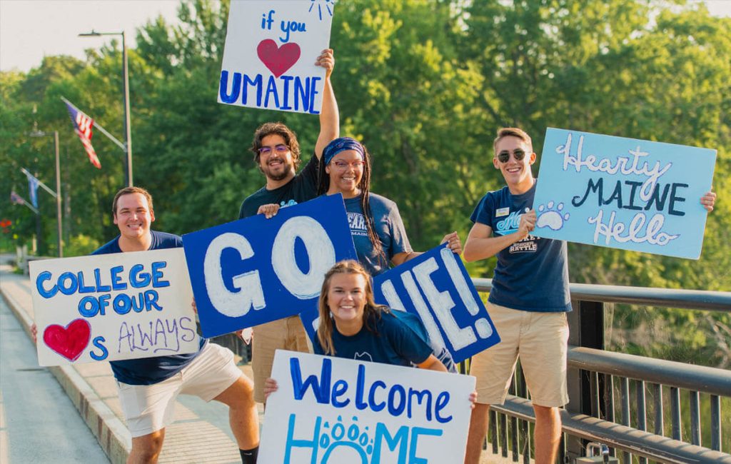 A photo of Team Maine members standing with signs welcoming new students to UMaine
